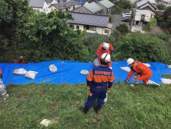 シートや土のうで崩落防止に取り組む消防団員の写真